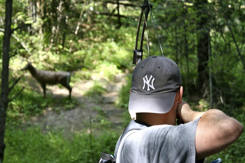 young man aiming a bow at a fake deer