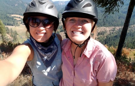 Two women with helmets taking a selfie on the hilltop.