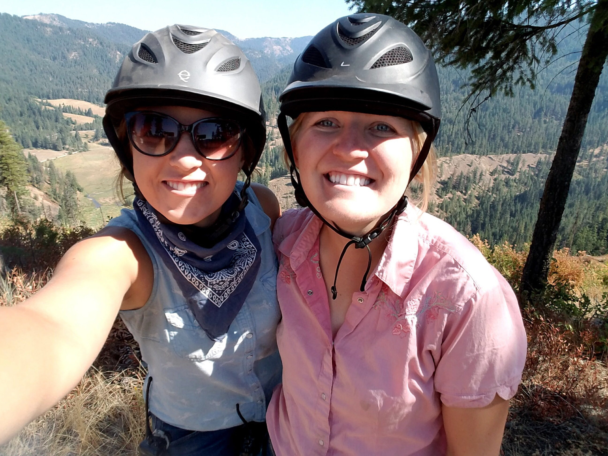 Two women with helmets taking a selfie on the hilltop.