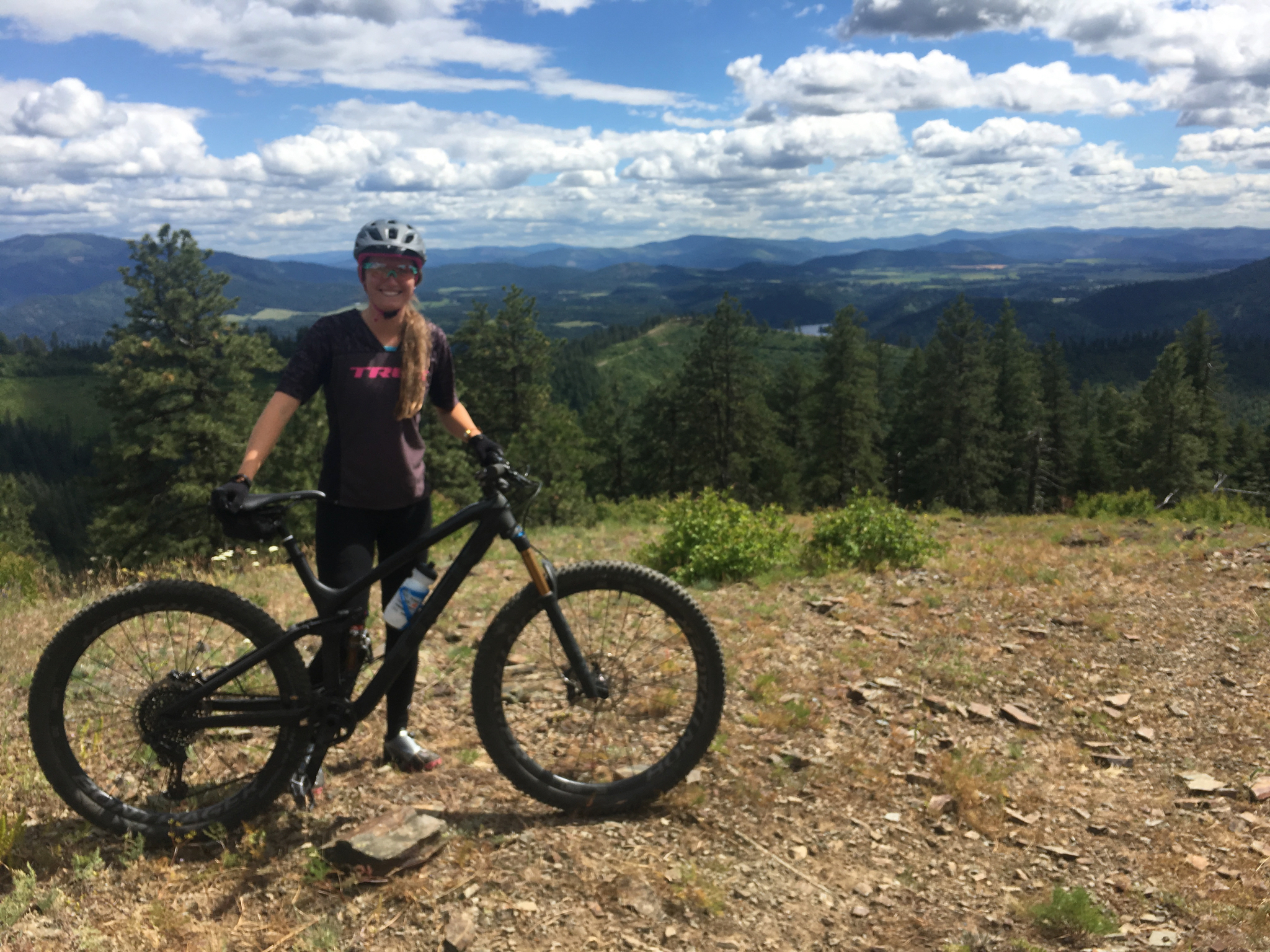 Woman posing with mountain bike on a hlltop.