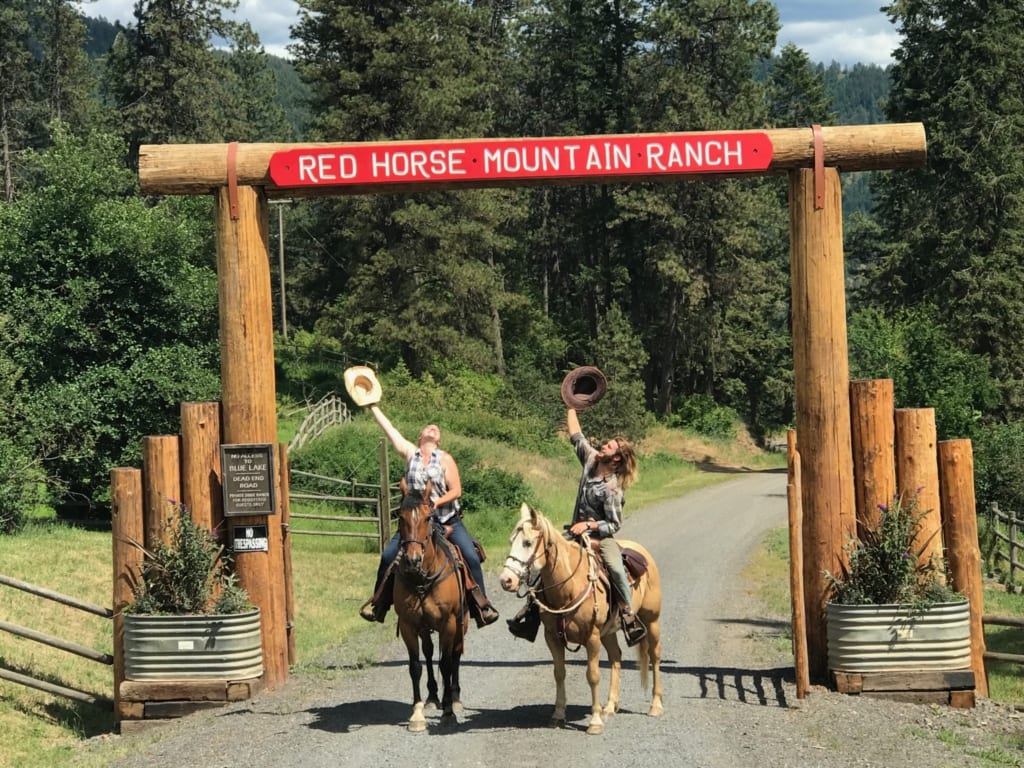 People on horseback under the ranch entrance sign posing for their all-inclusive horseback riding vacation.