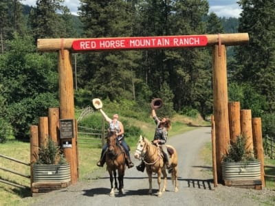 People on horseback under the ranch entrance sign.