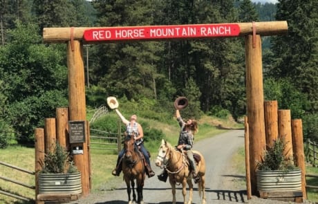 People on horseback under the ranch entrance sign.