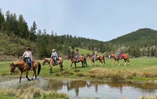 A group of horseback riders mosey through an alpine meadow at Red Horse Mountain Ranch.