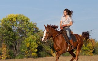 Benefits of Horseback Riding: A young woman smiles as she rides a horse amid the countryside.