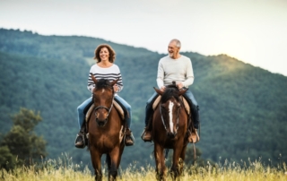 All-Inclusive Dude Ranch Adults Only: A senior couple rides horses amid a mountainous Idaho dusk.
