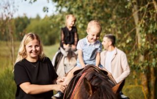 Ranch Vacation: A young woman and man smile while taking youngsters along a guided horseback ride.