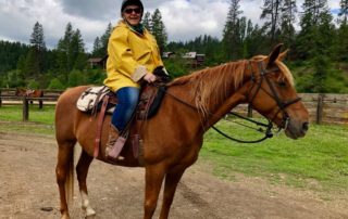 Dude Ranch Idaho: A woman wearing a yellow rain jacket happily mounts a brown horse.