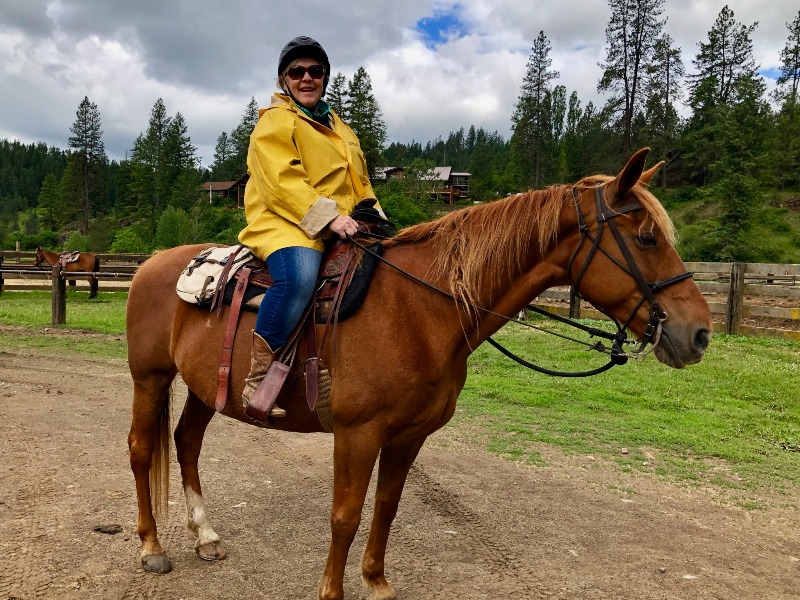 Dude Ranch Idaho: A woman wearing a yellow rain jacket happily mounts a brown horse.