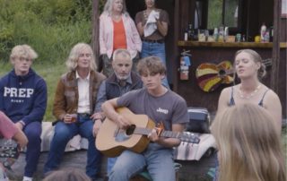 Multi-Generational Vacation: A young teen strums a guitar while his family sings in unison.