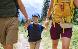 Family Adventure Vacations: A young boy smiles while wearing a pair of sunglasses and holding hands with and walking in-between his parents.