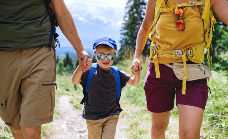 Family Adventure Vacations: A young boy smiles while wearing a pair of sunglasses and holding hands with and walking in-between his parents.