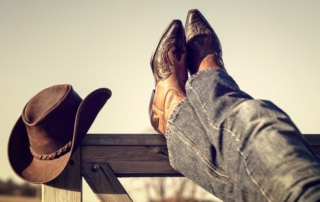 Dress in Western Style: A pair of legs with jeans and cowboy boots rests upon a gate alongside a traditional cowboy hat at Red Horse Mountain Ranch.