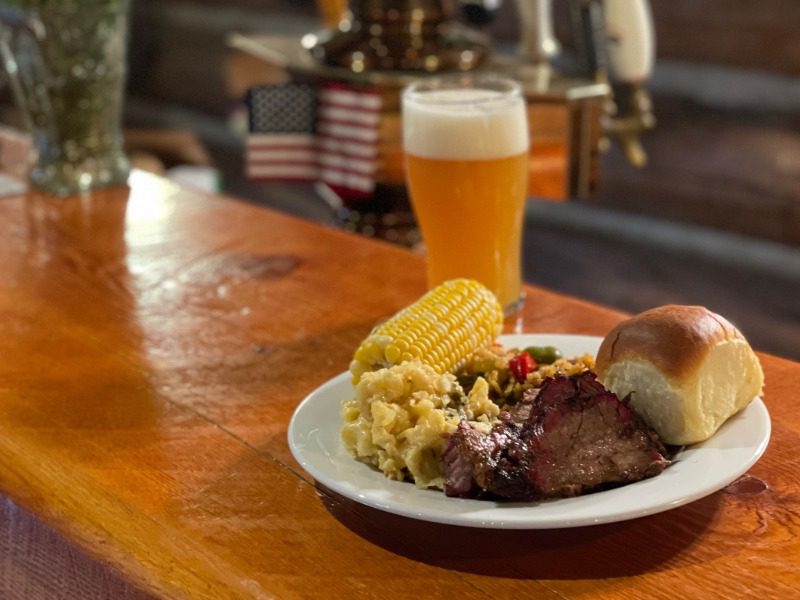 All-Inclusive Dining Experience: A plate of quintessential American food including prime rib, macaroni and cheese, a roll, and a tall glass of IPA.